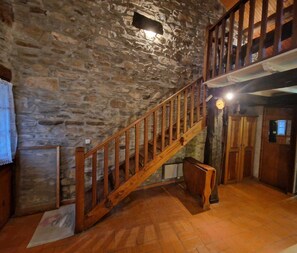 A rustic interior with a stone wall, wooden staircase, and a kitchen area. - Gîte 42 - LACAUNE - Gîte (LACAUNE)