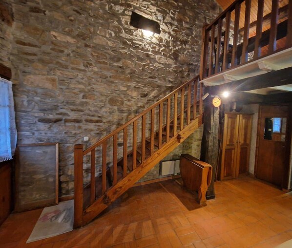 A rustic interior with a stone wall, wooden staircase, and a kitchen area.