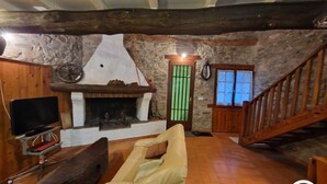 A rustic room with a stone wall, a fireplace, a wooden staircase, and a television. - Gîte 42 - LACAUNE - Gîte (LACAUNE)