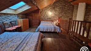 A cozy attic bedroom with two beds, a stone wall, wooden beams, and a skylight. - Gîte 42 - LACAUNE - Gîte (LACAUNE)