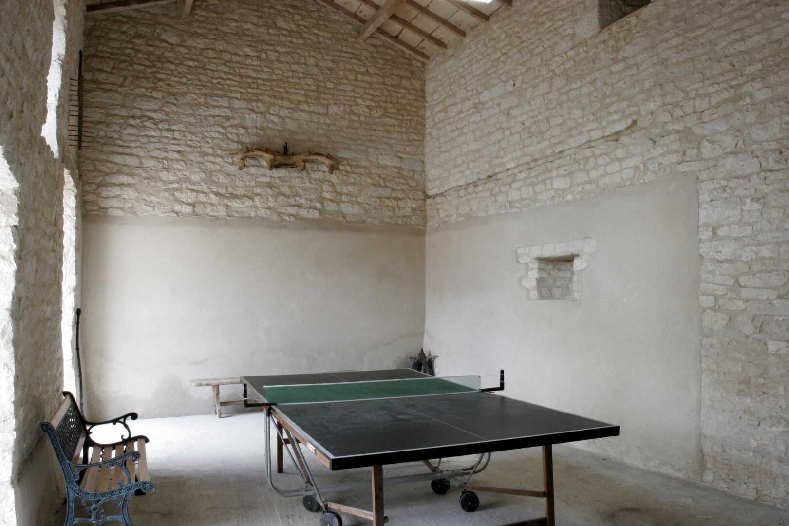 A room with a ping pong table, a bench, and stone walls.