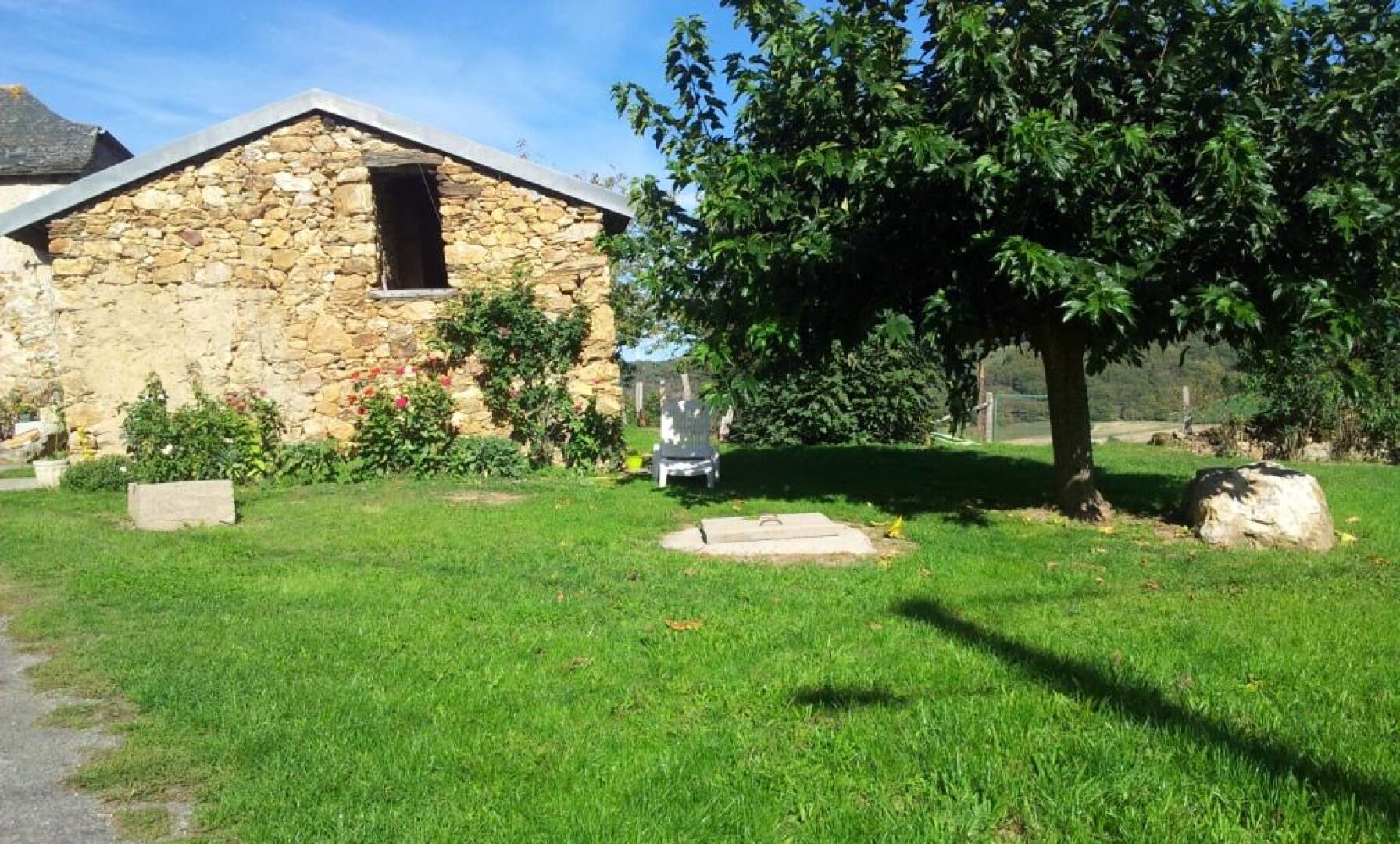 Un bâtiment en pierre doté d’un toit en pente, entouré d’une pelouse bien entretenue et d’un grand arbre.