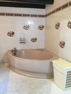Ein Badezimmer mit freistehender Badewanne, weißen Fliesenwänden mit floralem Muster, einem weißen Wäschekorb und einem schwarzen Deckenbalken.
