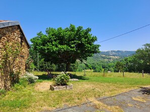 Ein Steinhaus mit einem Baum davor und einer Aussicht auf sanfte Hügel in der Ferne.