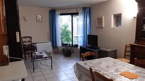 Un coin repas comprenant une table, des chaises, un téléviseur et une fenêtre avec des rideaux.