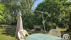 Un espace extérieur aménagé avec une table et deux chaises, entouré d’une végétation luxuriante et d’arbres.