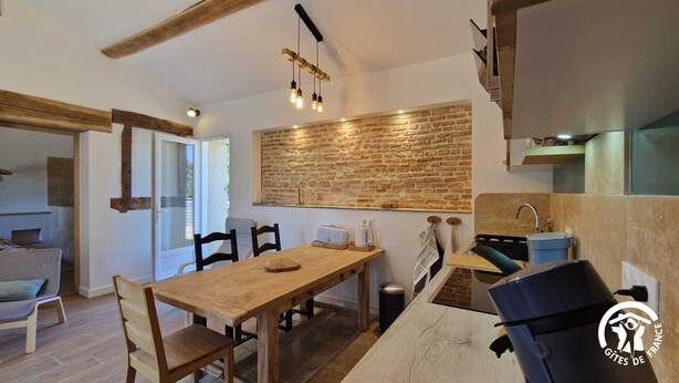 A modern kitchen with a wooden table, chairs, and a brick wall. - Le Chinchilla - GAILLAC (GAILLAC)