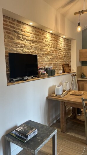 A modern kitchen with a stone wall, a flat-screen TV, wooden furniture, and a small table with magazines.