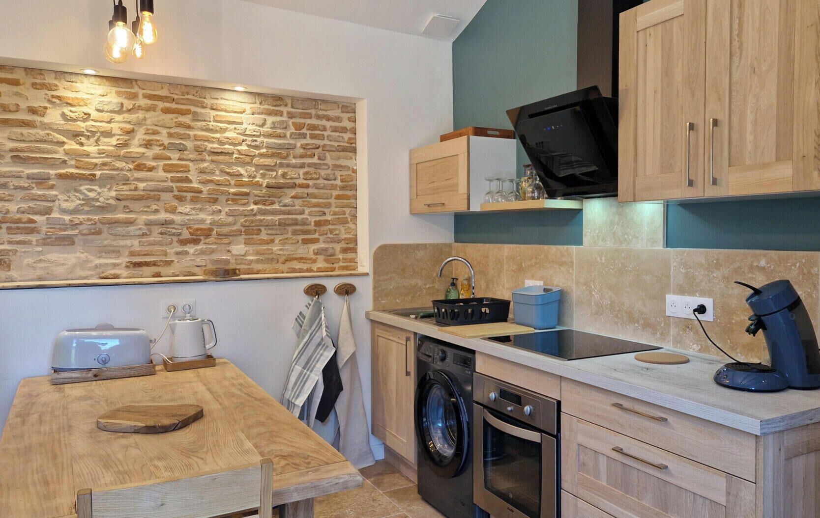 Cocina compacta con pared de piedra, armarios de madera, lavadora y horno empotrado.