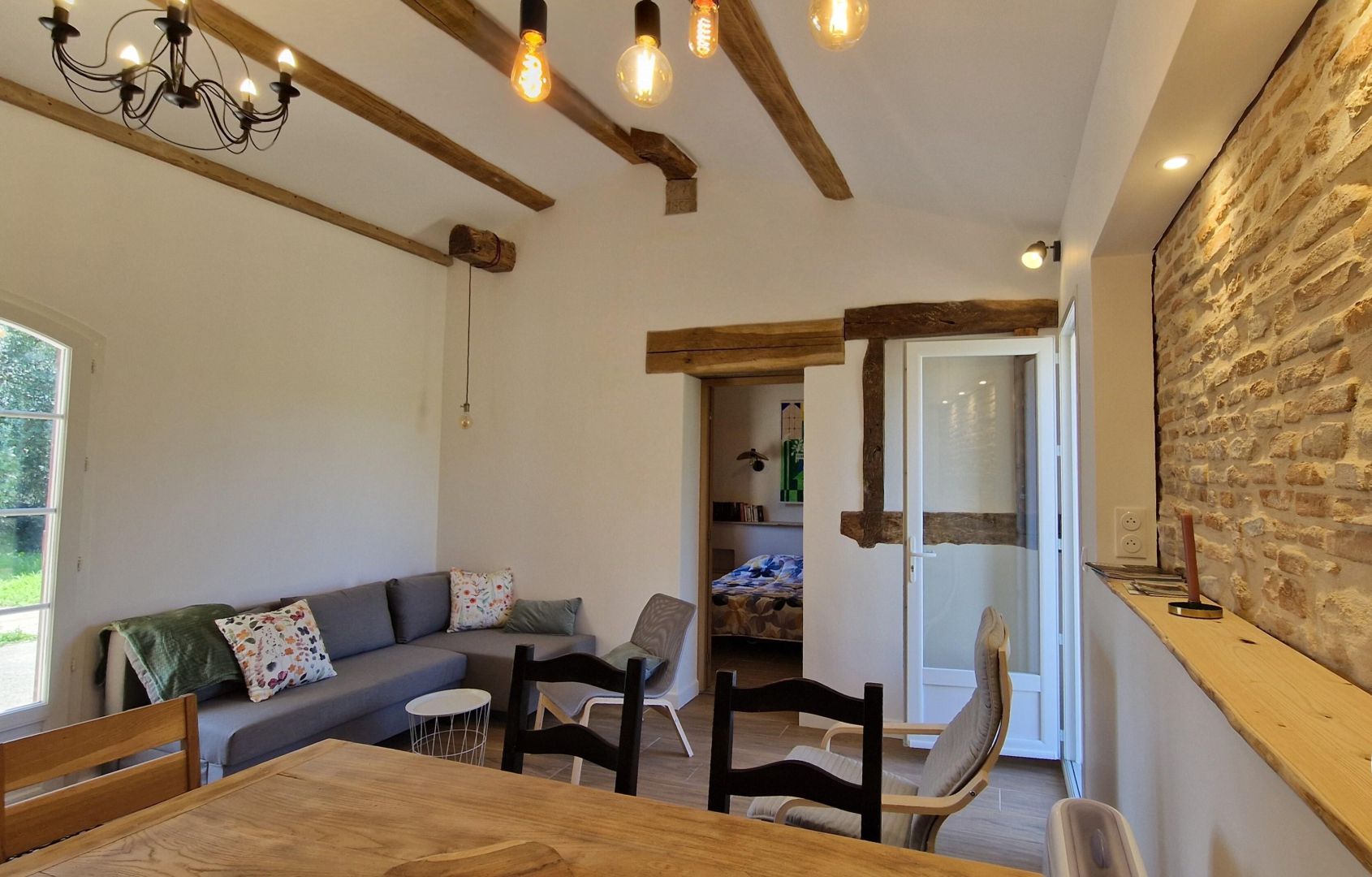A cozy living room with a wooden dining table, a sofa, and a stone wall.