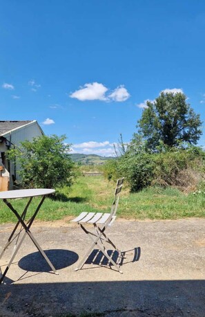 An outdoor seating area with a table and chairs, a wooden bench, and a view of a green landscape with trees and hills.