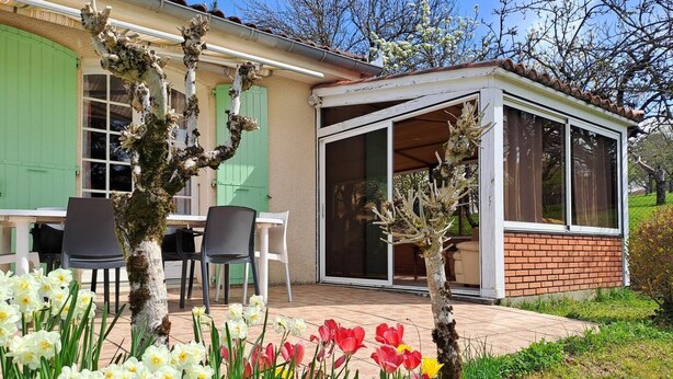 Uma casa com um espaço de pátio, uma mesa de jantar e cadeiras, e diversos tipos de flores.