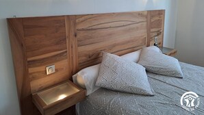 Quarto com cabeceira de madeira, duas mesas de cabeceira com abajures e roupa de cama estampada.