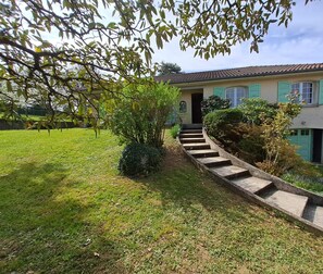 Una casa de dos pisos con una escalera de piedra que conduce a la puerta principal, rodeada de césped y arbustos cuidados.