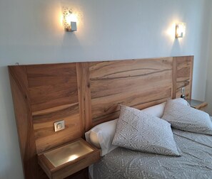 Un dormitorio con cabecera de madera, dos mesitas de noche con lámparas y ropa de cama estampada.