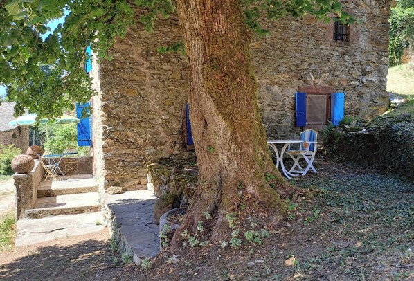 A rustic stone building with a tree in front, a small outdoor seating area, and a staircase leading to the entrance. - Cambert - MURAT-SUR-VEBRE (MURAT-SUR-VEBRE)