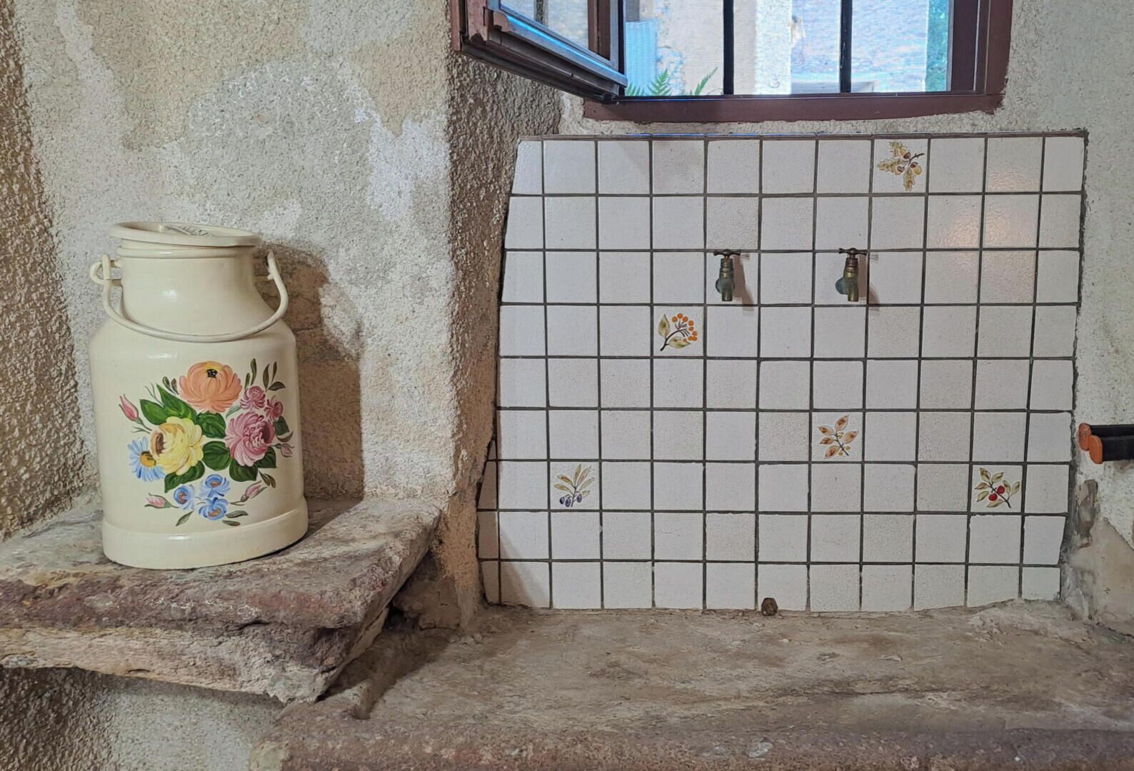 A tiled wall with a floral-patterned pitcher on a stone ledge.