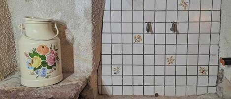 A tiled wall with a floral-patterned pitcher on a stone ledge.