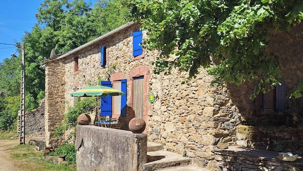 A rustic stone building with a wooden door, a small porch, and a satellite dish.