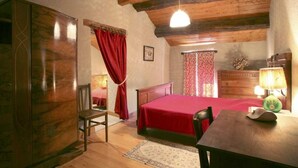 A bedroom with a wooden ceiling, a bed with a red bedspread, a wooden dresser, a chair, and a table with a lamp.