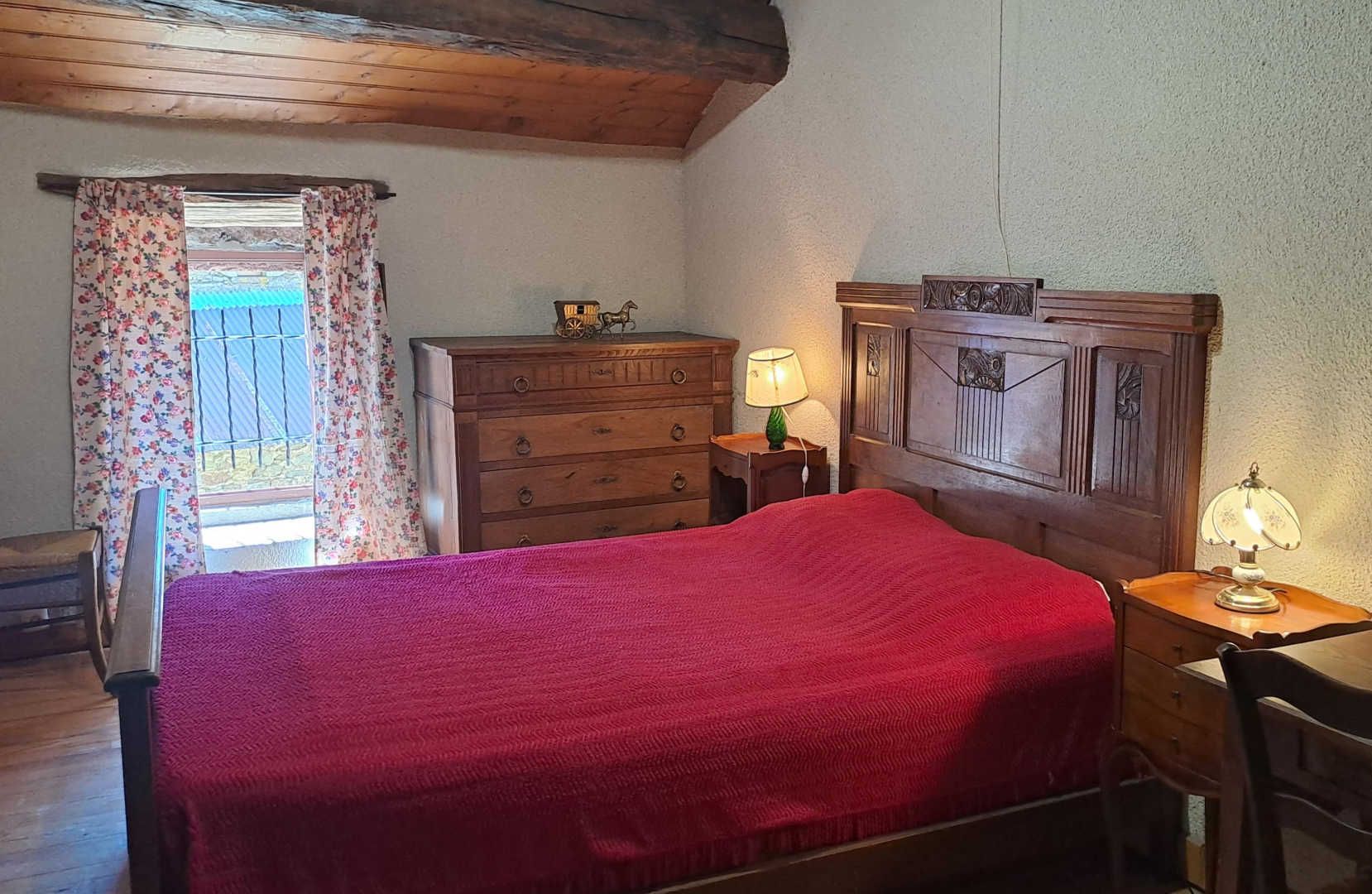 A bedroom with a wooden bed, a dresser, a nightstand with a lamp, and a window with floral curtains.