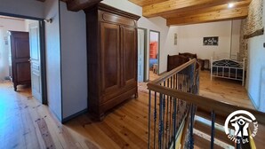 A spacious room with wooden floors, a large wardrobe, a staircase with a metal railing, and a bed with a white frame.