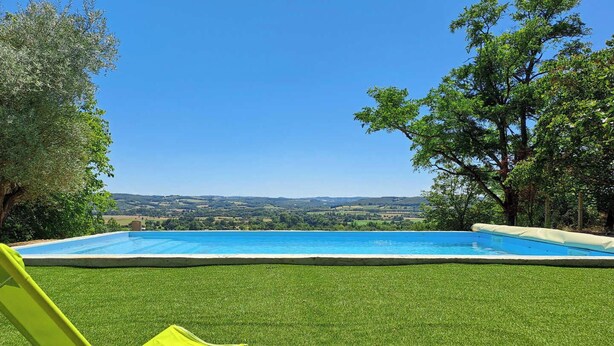 A swimming pool with a clear view of the landscape, a grassy area, and a yellow chair.