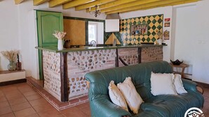 A cozy living room with a green sofa, a stone fireplace, and a kitchen area with a green door and yellow beams.
