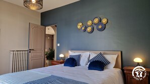 Une chambre à coucher comprenant un lit, des tables de chevet, un élément décoratif fixé au mur et un radiateur.