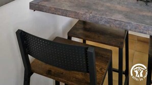 Une cuisine dotée d’un grand îlot central, de deux tabourets de bar, d’un luminaire suspendu et d’une plante en pot.