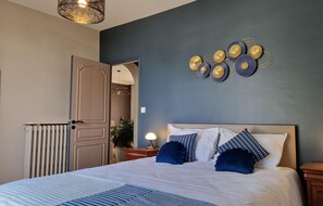 A bedroom with a bed, bedside tables, a wall-mounted decorative piece, and a radiator.