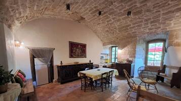 Un'area pranzo rustica con soffitto in pietra, un tavolo con sedie e una cucina sullo sfondo.