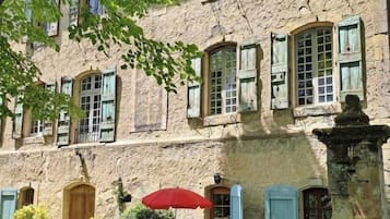 Un edificio con diverse finestre, un piccolo spazio esterno con un ombrellone rosso e un pilastro in pietra.