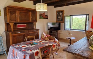A cozy dining area with a wooden table set for two, a television, and a window with a view of greenery.