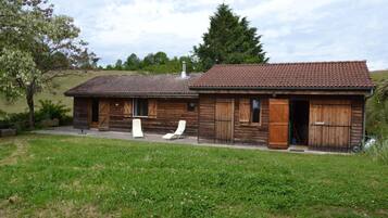 A rustic wooden house with a tiled roof, two open wooden doors, and a small porch with two white lounge chairs.
