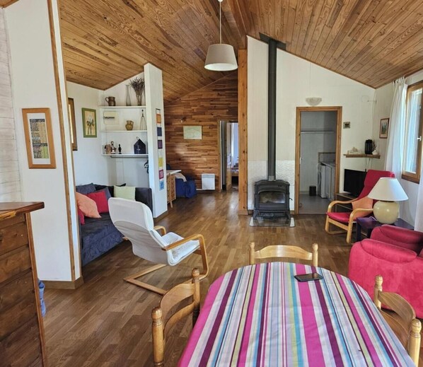 Un salon chaleureux avec une cheminée, un plancher en bois et un coin repas agrémenté d’une nappe à rayures.