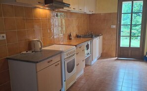 Une cuisine équipée d’une cuisinière, d’un four et d’un évier. Une fenêtre offre une vue sur la verdure environnante.