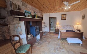 Une pièce confortable avec un lit, une chaise, une cheminée et un ventilateur de plafond.