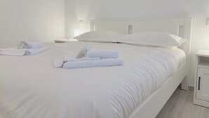 Ein ordentlich gemachtes Bett mit weißen Bettwäsche und Handtüchern, ein Nachttisch und ein kleiner Schrank.