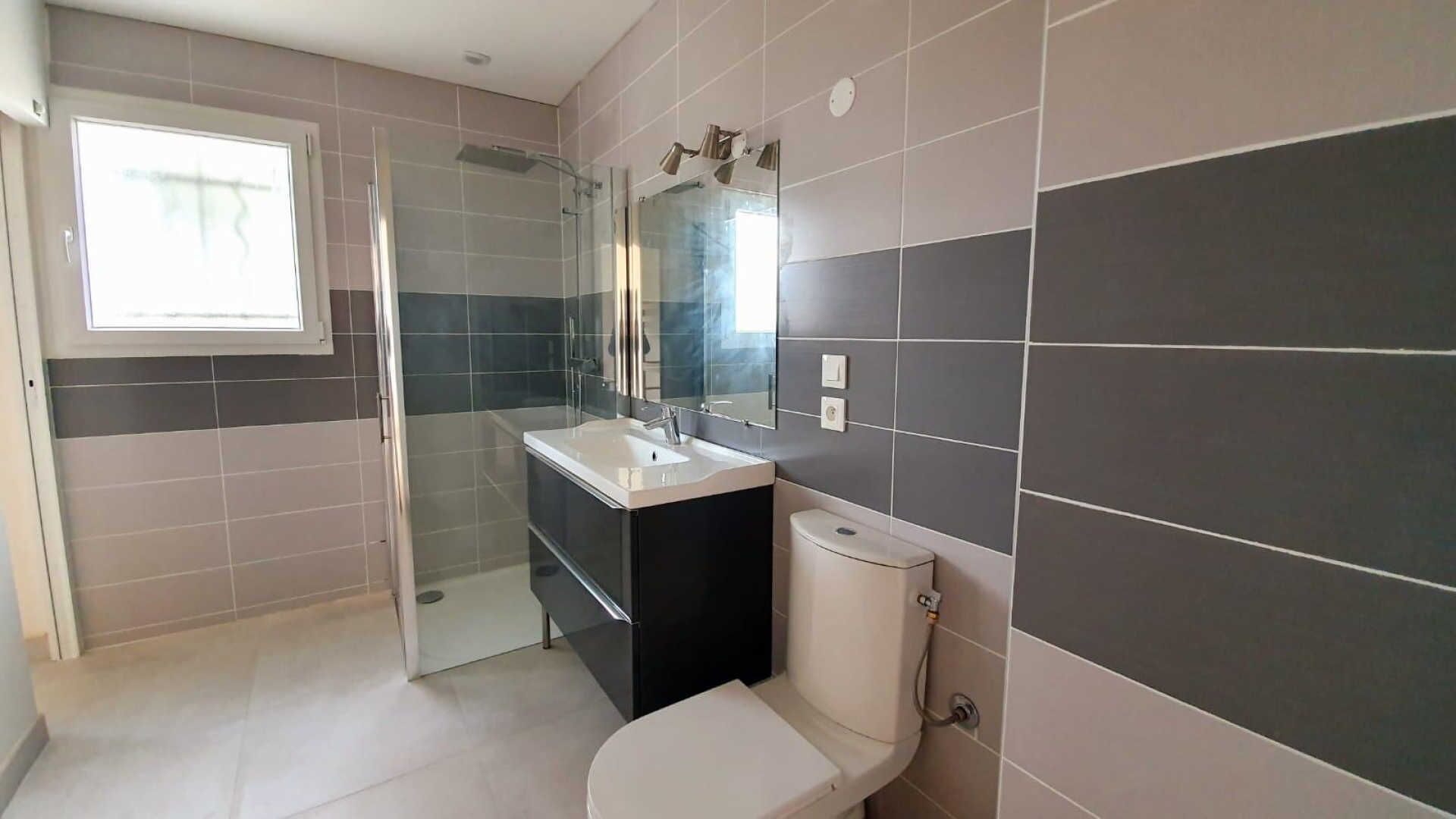 A bathroom with a shower, toilet, and sink, featuring a modern design with dark and light tiles.