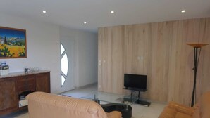 A modern living room with a wooden wall, a TV, and a floor lamp. - Les Acacias d'En Cassé (LAVAUR)