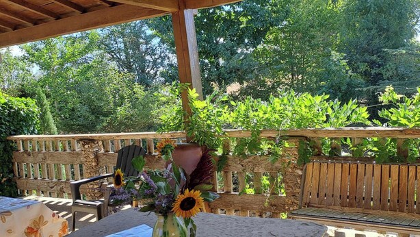 An outdoor patio with a wooden table, a chair, and a vase with flowers. - Au pré vert - SAINT PIERRE DE TRIVISY (SAINT PIERRE DE TRIVISY)