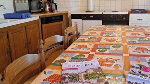 A kitchen with wooden cabinets, a white refrigerator, and a table with a colorful tablecloth and brochures. - Au pré vert - SAINT PIERRE DE TRIVISY (SAINT PIERRE DE TRIVISY)