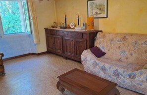 Un salon avec un canapé à motifs, un meuble en bois, une petite table et une fenêtre avec des rideaux.