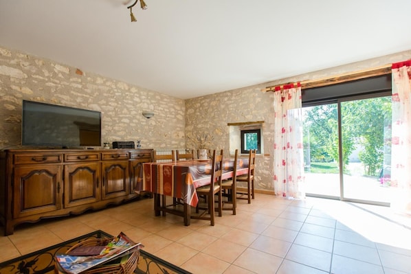 A dining area with a stone wall, wooden furniture, a flat-screen TV, and a view through a glass door.