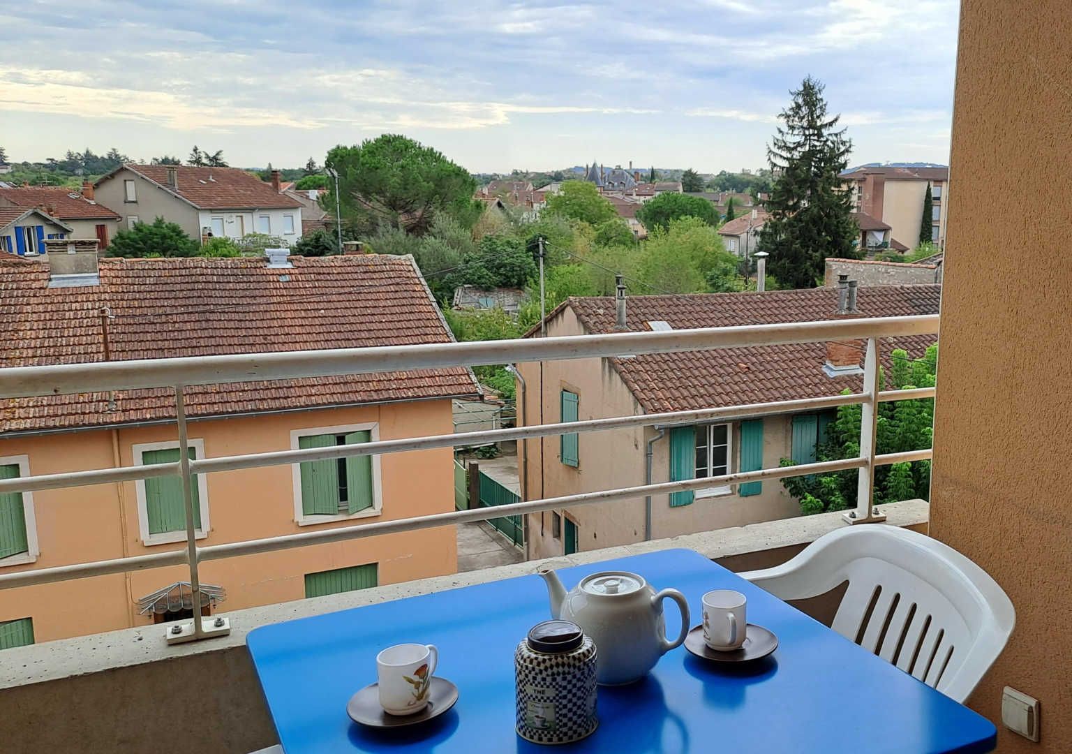 Un balcon avec une table dressée pour le thé, donnant sur un quartier résidentiel avec des maisons et des arbres.