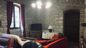 A stone-walled room with a fireplace, a television, a sofa, and a leather chair.