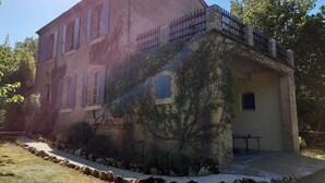 A two-story building with a stone facade, a balcony with a metal railing, and a small patio area with a table and chairs.