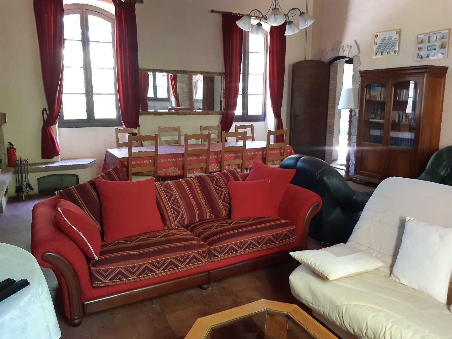 Un salon avec un canapé rouge, un canapé blanc, une table à manger avec des chaises et un buffet en bois.