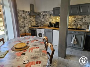 Een kleine keuken met een betegelde spatwand, een wasmachine en een eethoek met een tafel gedekt voor twee personen.